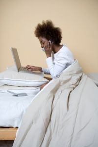 Woman using cell phone and laptop in bed,  side view