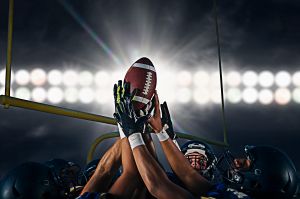 Victorious teenage and young male american football team holding up ball at night