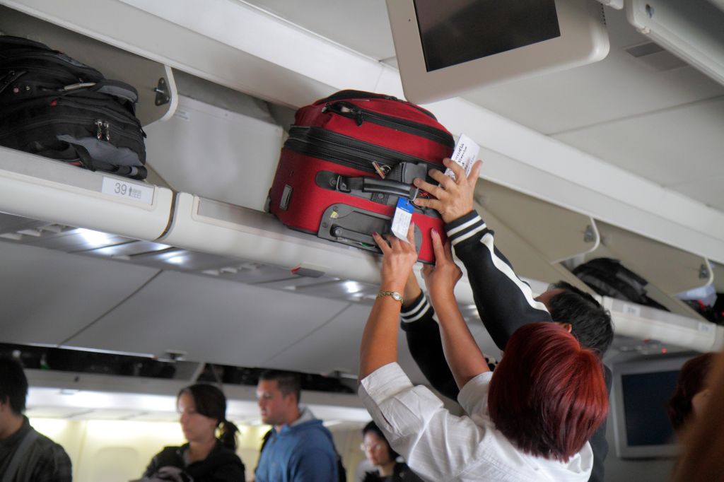 United commercial airliner cabin man woman overhead luggage bin suitcases