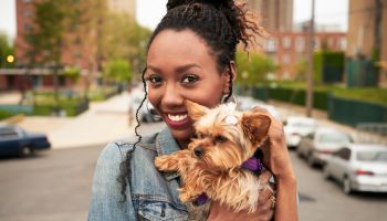 Black woman holding dog in city