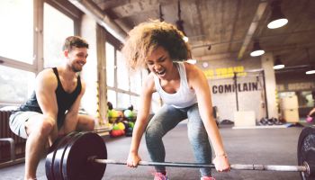Young woman with training partner preparing to lift barbell in gym