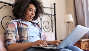 Woman lying in bed and using laptop at home