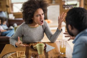 Angry African American woman arguing with her husband at dining table.