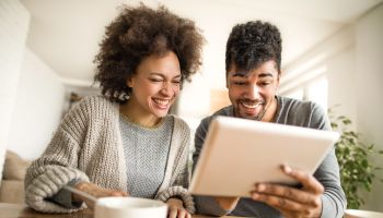 Happy black couple having fun while using touchpad at home.