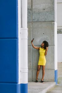 Fashionable businesswoman in yellow dress taking selfie with smartphone