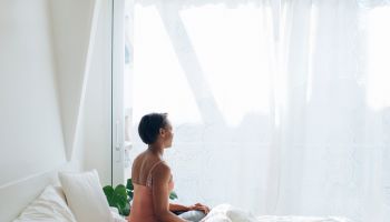 Woman sitting on bed at home looking out of window