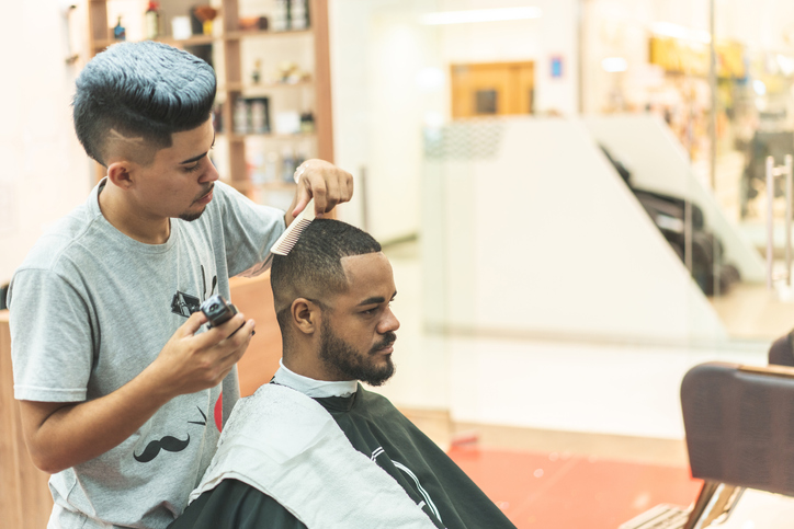 Getting haircut by barber, with electric trimmer at barbershop