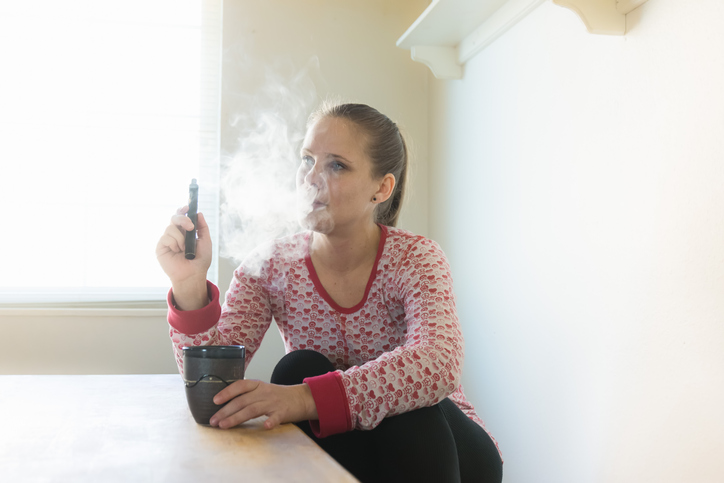 Women relaxing in the kitchen with a vape pen and a cup of coffee.