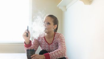 Women relaxing in the kitchen with a vape pen and a cup of coffee.