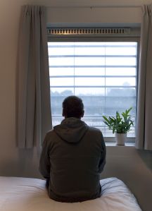 Rear View Of Man Looking Through Window At Home