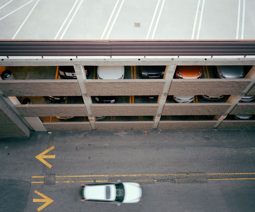 Car passing multi-story garage, overhead view (blurred motion)