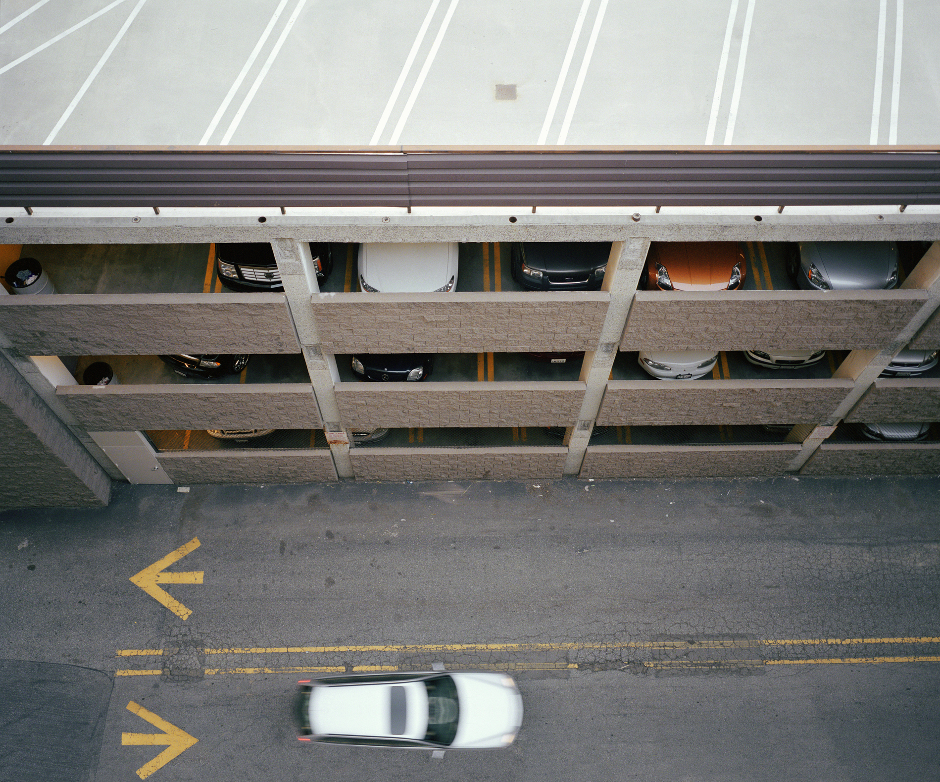 Car passing multi-story garage, overhead view (blurred motion)