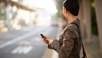 Businesswoman waiting on bus stop with smartphone