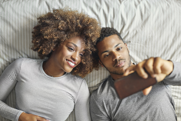 Smiling couple taking selfie while lying on in bed