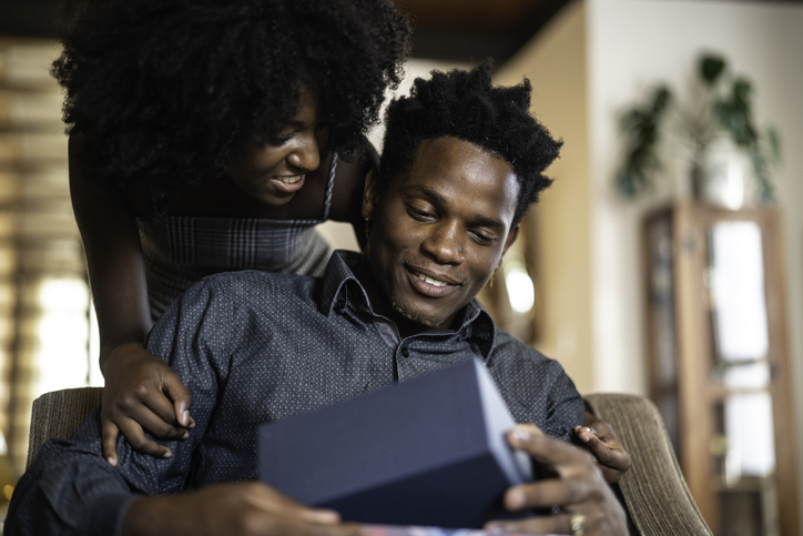 Wife making a surprise giving a present to her husband at home