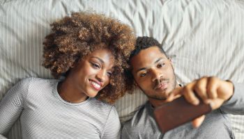 Smiling couple taking selfie while lying on in bed