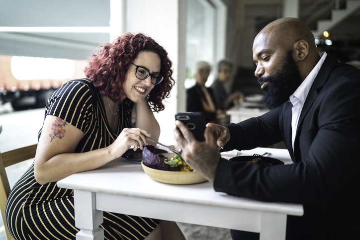 Man showing something in his smartphone to a friend / girlfriend in a restaurant