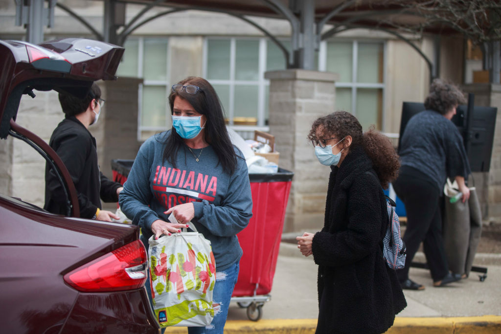 A mother in a mask helps move her daughter, a freshman, back...