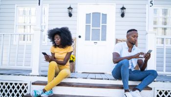 African couple sitting on stairs, having relationship problems, using smart phones