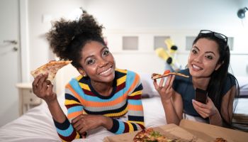 Girlfriends eating pizza in bed and watching TV stock photo