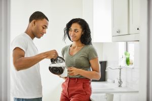 Woman looking at man pouring coffee in cup at home