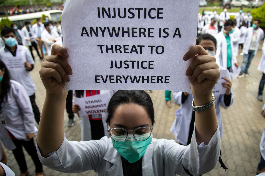 A doctor wearing a facemask holds out a protest placard...