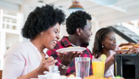 Latin family consisting of Latino man with brown skin and afro hair and two Latin women with brown skin and afro hair, one of them 52 and the other 29 are all sitting in a beautiful restaurant with typical Colombian food