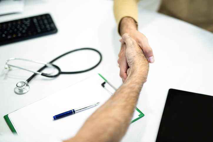 Patient and doctor shaking hands close up.