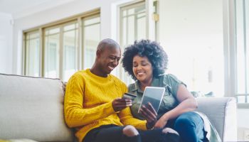 Smiling couple sitting on their living room sofa and using a tablet