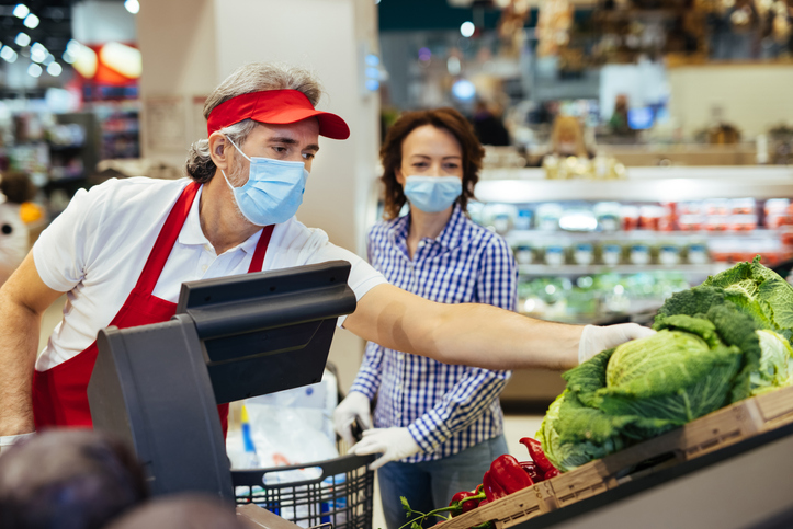 Supermarket employee helping a customer choose vegetable during coronavirus pandemic