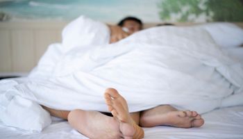 Shot of couple's feet poke out of the bottom of a duvet in bed.