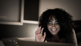 Young woman waving while doing a video call on laptop lying in bed at home