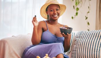 Portrait of a young beautiful woman wearing a sunhat and having breakfast on the sofa at home