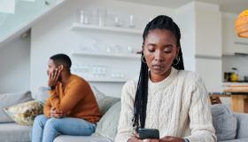 Shot of a young woman ignoring her partner while using a cellphone at home