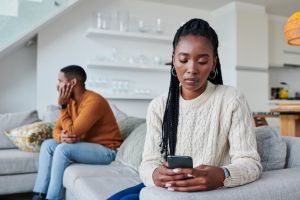 Shot of a young woman ignoring her partner while using a cellphone at home