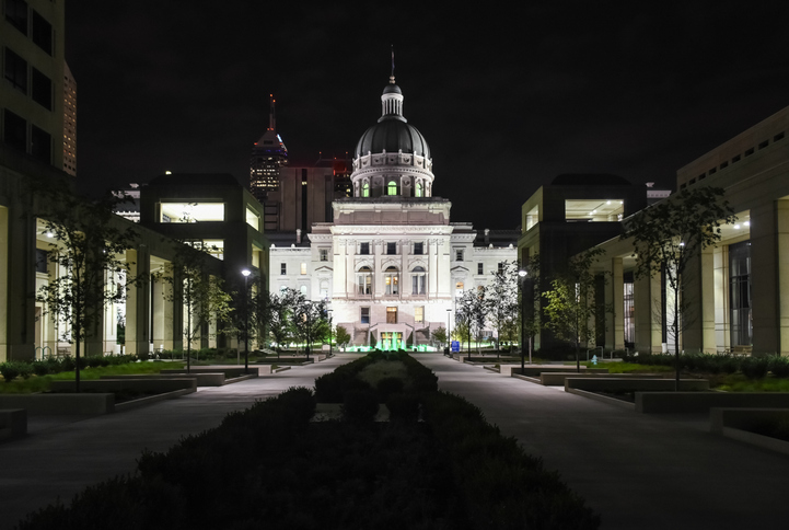 Majestic Indiana State Capitol building facade brightly illuminated at night with skyscrapers on background in Indianapolis, Indiana, USA