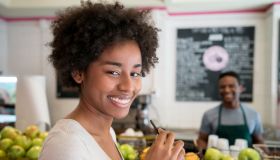 Portrait of a beautiful african american customer at a juice bar looking at camera smiling and salesman standing at the background