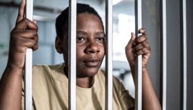 Young afro woman looking serious and desperate behind bars which may be prison bars or those of a security gate