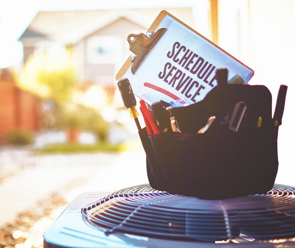 Air conditioning unit with a work bag of tools on top and a reminder to schedule a service