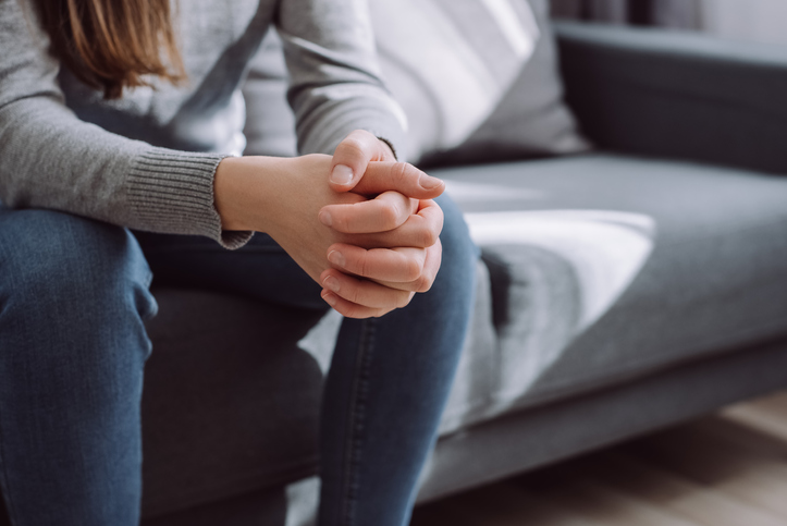 Unrecognizable female folded hands on knees together, sitting on couch alone, upset depressed girl feeling lonely, suffering from domestic violence or relationship problem, break up with boyfriend