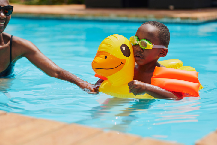 Mother, black family and kid learning swimming in pool, having fun and bonding. Mom love, education and happy mama teaching child or boy how to swim in water, training and exercise on duck floater.