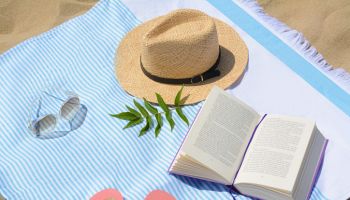 Beach towel with book, straw hat, sunglasses and flip flops on sand