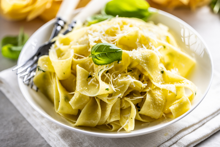 Homemade pasta Pappardelle with olive oil basil and parmesan cheese. Italian pasta Aglio e Olio in white plate on kitchen table.