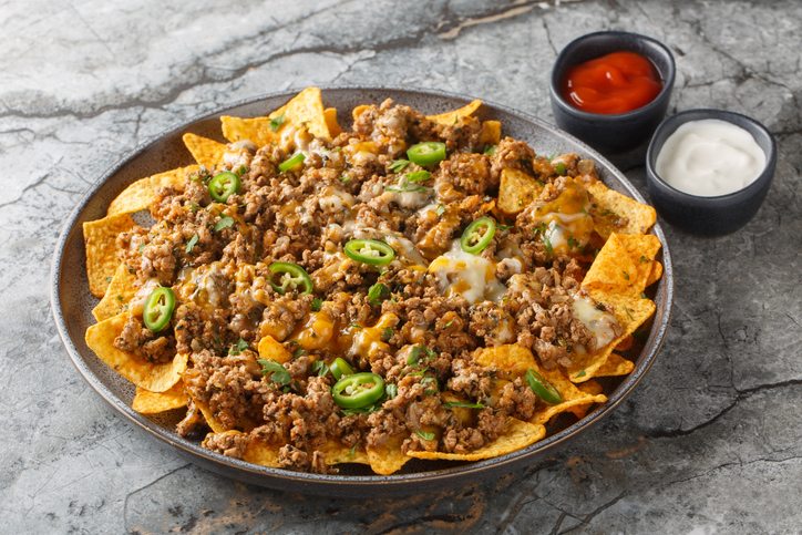 Ground Beef and Cheese Nachos with jalapeno peppers, herbs and sauces closeup on the plate. Horizontal