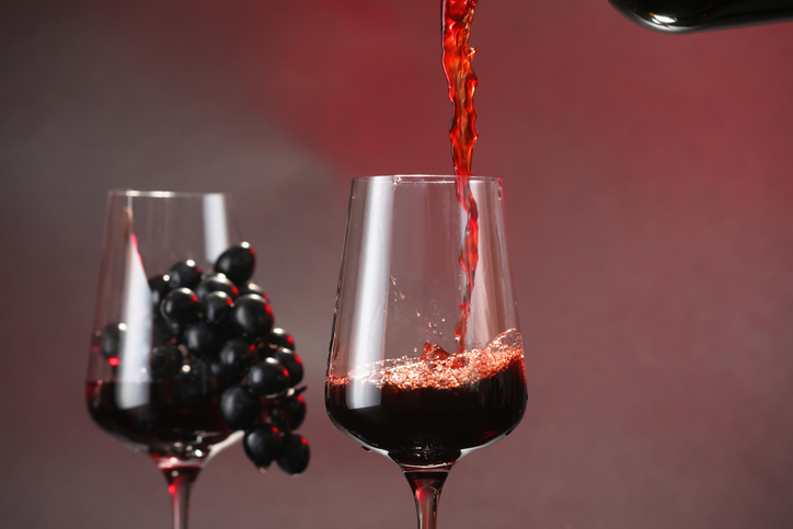 Pouring red wine into glass on color background, closeup