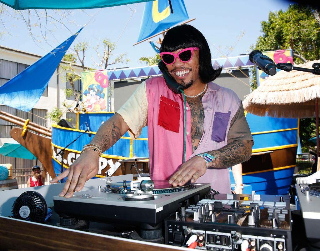 A person wearing sunglasses and a colorful outfit is operating DJ equipment at an outdoor event with festive decorations.