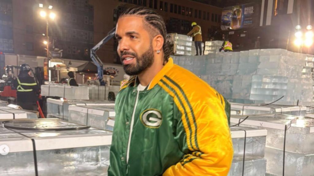 A man wearing a Green Bay Packers jacket standing in front of a large ice sculpture at night.