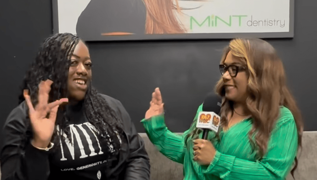 Two women, one wearing a "MINT dentistry" logo shirt, are being interviewed and gesturing animatedly.