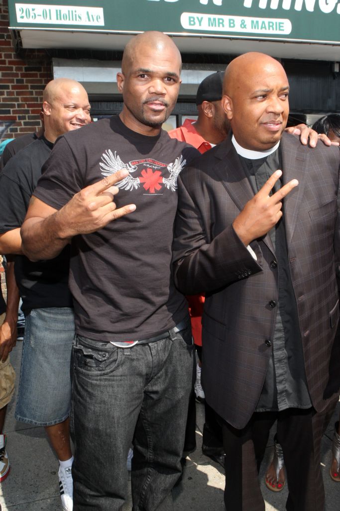 Three African American men, one wearing a Red Hot Chili Peppers t-shirt, standing together in front of a sign that says "205-01 Hollis Ave BY MR B & MARIE".