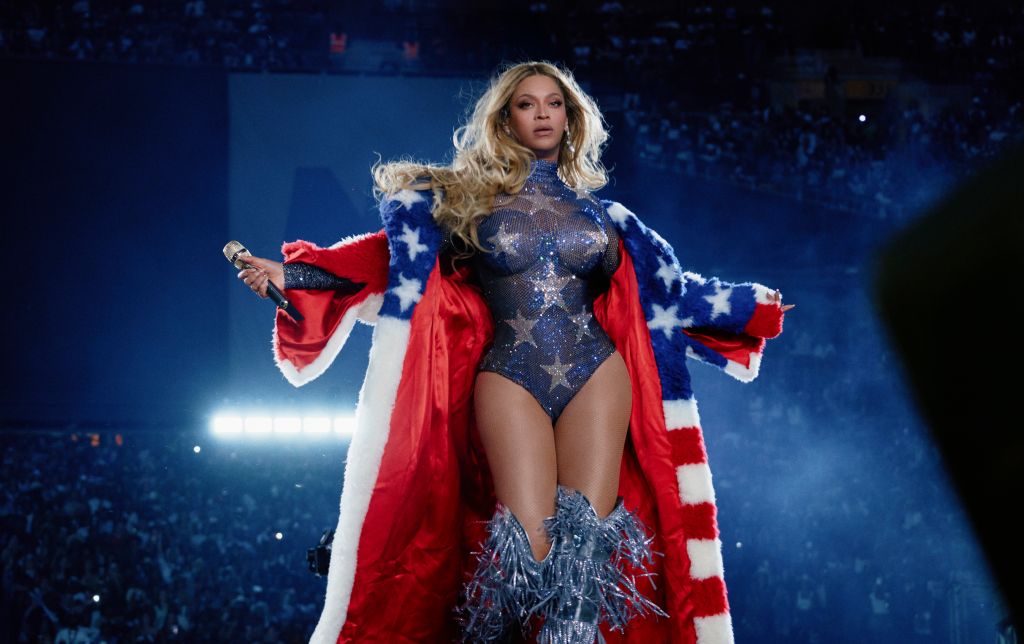 A woman wearing a red, white, and blue star-spangled costume performs on a stage with a blue backdrop and bright lights.